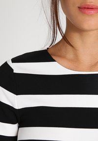 Czarna i biała bluzka w paski z okrągłym dekoltem, wykonana z gładkiego materiału, z naprzemiennymi szerokimi paskami o równej szerokości.