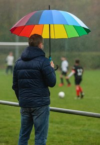 Buntes, achtteilige Regenschirm mit roten, orangefarbenen, gelben, grünen, blauen und lila Abschnitten, gehalten von einer Person in einer dunkelblauen Daunenjacke.