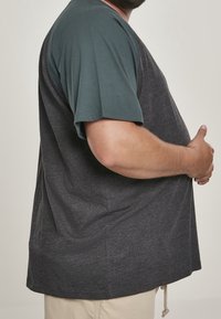 T-shirt z raglanowymi, krótkimi rękawami w ciemnoszarym kolorze z miętowym kołnierzem. Miękka bawełniana mieszanka materiałów, o luźnym kroju i zaokrąglonym dole.