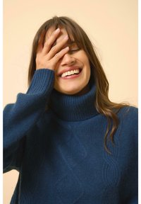 Modrý pletený svetr s vysokým rolákem, zdobený texturovaným vzorem a žebrovanými manžetami. Měkká, teplá látka s uvolněným střihem.