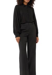 Black long-sleeve shirt with button closure, featuring a soft fabric and gathered detailing on the sleeves, paired with tailored black pants.