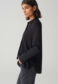 Maglietta nera a maniche lunghe con collo, texture morbida, fit largo e orlo curvo, abbinata a jeans grigio scuro.