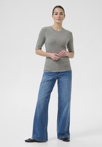 Grå tætsiddende t-shirt med korte ærmer, parret med løse blå denim wide-leg jeans. Outfittet suppleres af sorte flade sko.