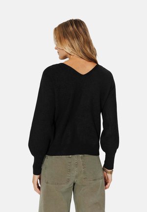 Un pull noir en tricot avec un col en V et des manches ballon, associé à un pantalon vert avec des poches latérales et une coupe décontractée.