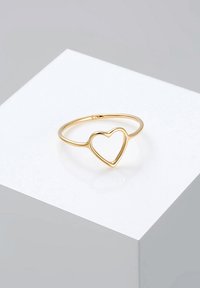 Goldener Ring mit offenem Herzmotiv. Dünner Band mit glatter, glänzender Oberfläche, präsentiert auf einer hellen Fläche.