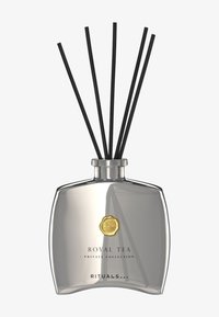 Dyfuzor zapachowy z metalicznie srebrną butelką, złotym emblematem i pięcioma czarnymi patyczkami. Charakteryzuje się zakrzywionym kształtem i minimalistycznym designem.