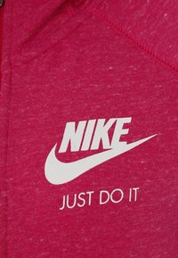 Haut de sport rose en tissu texturé, orné d'un logo Nike blanc et du slogan "JUST DO IT" imprimé en évidence sur le devant.