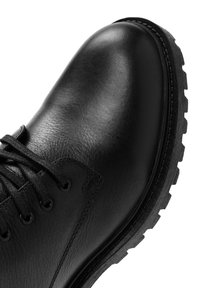 Botín de cuero negro hasta el tobillo con puntera redondeada, superficie texturizada y suela de goma resistente. Presenta un diseño clásico de cordones y sencillos detalles de costura.