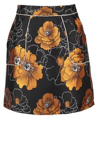 Jupe fleurie en tissu noir ornée de grands coquelicots orange. Elle présente une coupe ajustée avec deux poches avant bordées de passepoil blanc.