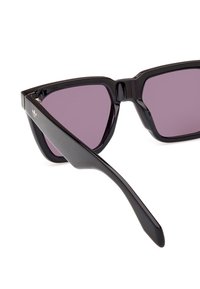 Ochelari de soare din plastic negru cu o formă geometrică, lentile violet și un logo subtil pe lateral. Brațe texturate pentru o prindere mai bună.