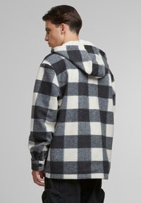 Camicia di flanella con motivo a quadri grigi e neri, design con cappuccio e polsini con bottone, che mostra una texture morbida e una vestibilità comoda.