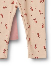 Béžové legíny z žebrované látky s malým červeným květinovým potiskem a růžovou vnitřní podšívkou viditelnou skrz šev u nožního otvoru.