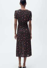 Schwarzes Blumenkleid mit kurzen Puffärmeln und einer Länge bis zur Mitte der Wade. Merkmale sind eine taillierte Passform, subtiler Glanz und kleine rote Blumen überall.