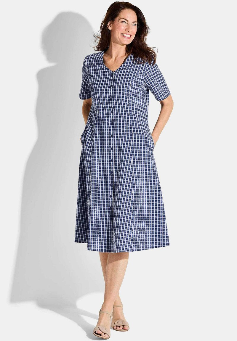 Abito in gingham blu navy e bianco con maniche corte, scollatura a V, chiusura frontale con bottoni, orlo svasato e tasche laterali. Tessuto di cotone morbido.