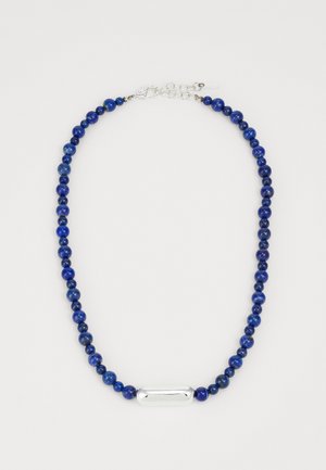 Zila lapis lazuli pērlīšu kaklarota ar sudraba ovālizemu akcentu, piedāvājot bumbu un ķēdes aizdari. Pērlītes ir dažādās izmēros, radot teksturētu izskatu.