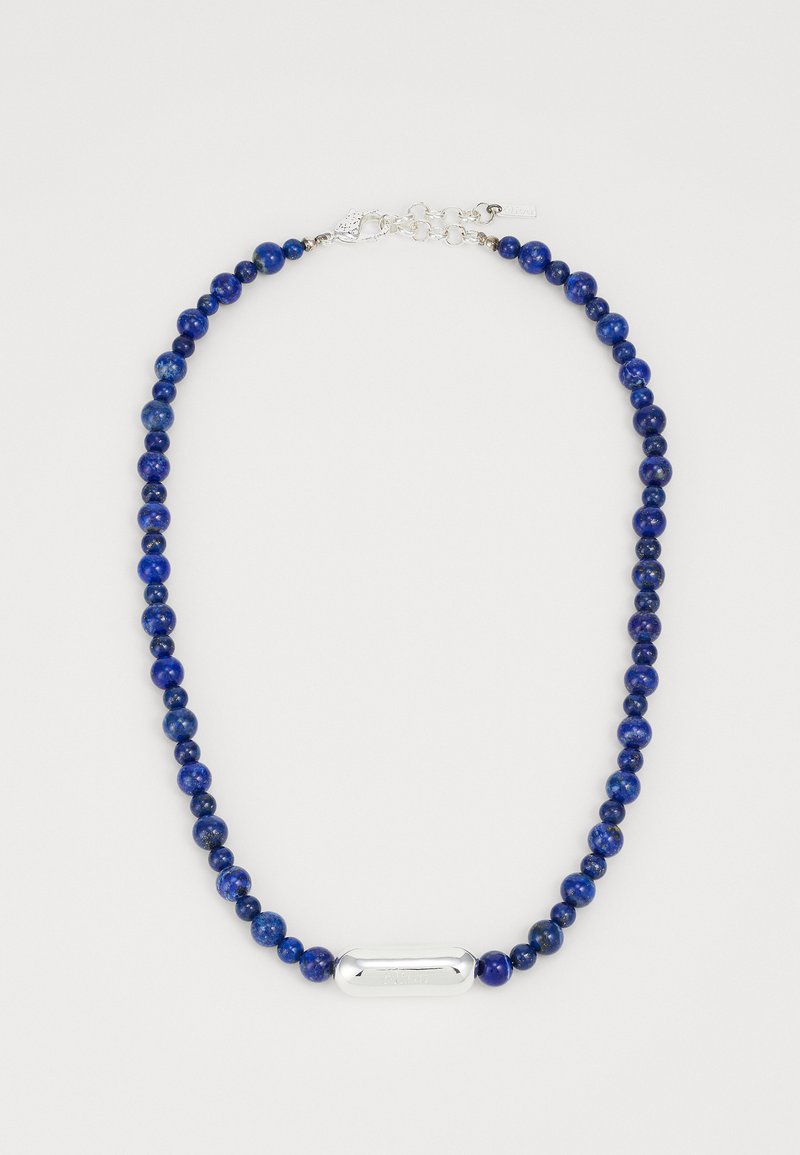 Κολιέ από μπλε λαπις λαζουλί με ασημένιο οβάλ στοιχείο, διαθέτει κλείσιμο τύπου μπάλα και αλυσίδα. Οι χάντρες διαφέρουν σε μέγεθος, δημιουργώντας μια υφητική εμφάνιση.