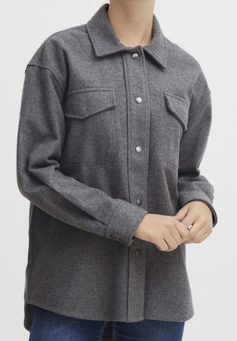 Szara koszula-kurtka z mieszanki wełny, z kołnierzem, zatrzaskami i dwoma kieszeniami na piersi. Posiada luźny krój i długie rękawy.