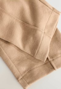 Beigefarbener Strickstoff, dicht gewebt mit einer glatten Textur. Verfügt über flache Nähte und einen umgeschlagenen Saum, der ein sauberes, minimales Design unterstreicht.