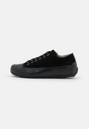 Zapatilla negra de corte bajo con cierre de cordones, combinación de cuero liso y ante, y suela de goma texturizada sobre un fondo blanco.