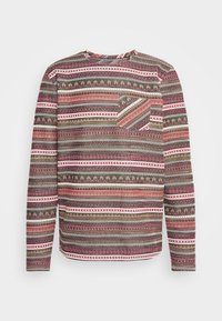 Camicia a maniche lunghe in un tessuto con texture, caratterizzata da un motivo geometrico rosso, marrone e crema, con una tasca sul lato sinistro del petto. Collo tondo.