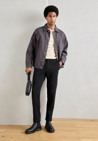 Gray cotton jacket, beige crew neck shirt, black sweatpants, black ankle boots, holding a black shoulder bag. Casual, modern outfit.