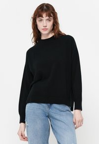 Pull en maille noir avec un col montant, coupe décontractée et épaules tombantes. Assorti à un jean déchiré bleu clair. Design minimaliste.