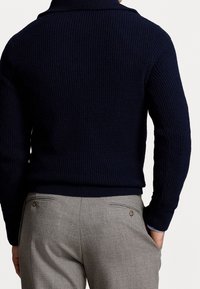 Mörkblå stickad tröja med en tjock, ribbad textur och krage. Kombinerad med ljusgrå byxor med två bakfickor och knappar.