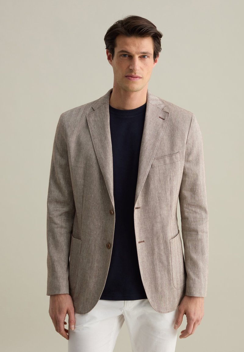 Blazer en lin marron clair avec une finition texturée, design à un bouton, revers crantés et deux poches avant, porté sur une chemise bleu marine.