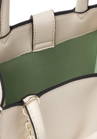 Bolso texturizado beige con un forro interior verde, con bordes negros y acentos de hardware dorado. Muestra el diseño interior abierto del bolso.