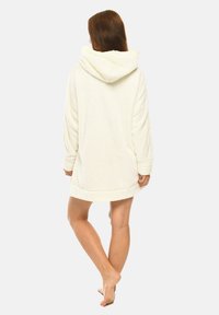 Hooded oversized robe in soft white fabric, featuring a textured exterior, long sleeves, and a rounded hem. Simple and cozy design.
