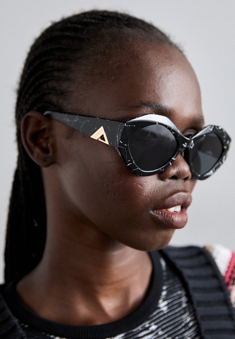 Black cat-eye sunglasses with a marbled texture and gold hardware detail at the temple. Lenses are dark and slightly reflective.