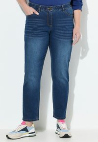 Dunkelblaue Jeans aus Denim mit geradem Bein, Fronttaschen und sichtbaren Nähakzenten; kombiniert mit mehrfarbigen Sneakers.