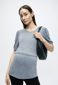 Γκρι πλεκτό τοπ με κοντά φουσκωτά μανίκια, με οριζόντια ραφή. Συνδυάζεται με μαύρη τσάντα ώμου με λεία υφή.