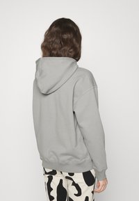 Felpa con cappuccio grigia dal taglio morbido e polsi a costine, abbinata a pantaloni a righe bianchi e neri. Design semplice e texture morbida.