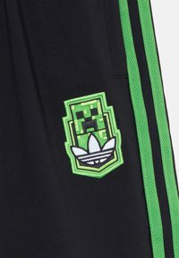Black shorts with green side stripes, featuring a dual-colored embroidered badge with a pixelated character and stylized Adidas logo.