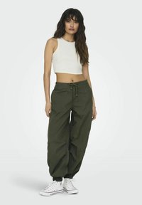 Witte tanktop met een ronde hals, gecombineerd met olijfgroene joggerbroeken met trekkoorden en witte sneakers met zwarte accenten.