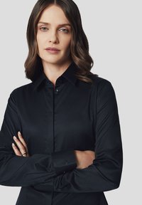 Czarna koszula z guzikami, wykonana z gładkiego materiału, z klasycznym kołnierzykiem, długimi rękawami oraz detalem logo na mankiecie.