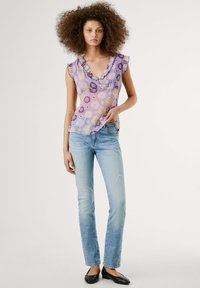 Violeta ziedu topiņš ar V veida kakla izgriezumu un volānu piedurknēm, saskaņots ar gaiši ziliem, nolietotiem džinsiem un melniem dzīvokļiem. Tekstūrēts audums un spilgtas apdrukas.