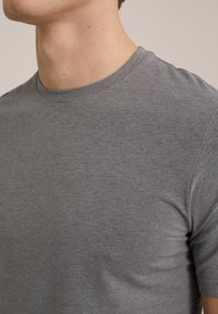 Camiseta de cuello redondo de manga corta en gris, hecha de tela suave, con una forma ajustada y textura lisa, con detalles de costura mínimos.