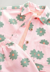Ljusrosa skjorta med grön blommönster och orange mittpunkter, med krage och knappstängning. Rosa elastisk midjeband på matchande shorts.