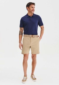 Granatowa koszulka polo, khaki szorty i beżowe trampki. Krótkie rękawy, klasyczny kołnierzyk oraz pleciony pasek dodają stylu do stroju.