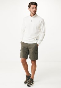 Vit kvart dragkedja pullover i mjukt material, ihop med olivgröna cargoshorts. Sportskor med mörka och ljusa accenter fulländar stilen.
