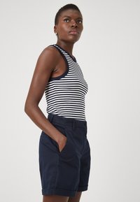 Pantaloni corti blu navy con risvolti, abbinati a una canotta aderente a costine con strisce orizzontali bianche e bordi blu navy.