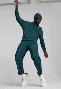 Sudadera azul con bolsillo tipo canguro y puños de canalé, combinada con pantalones azules que tienen costuras blancas. Zapatillas blancas con acentos de color.