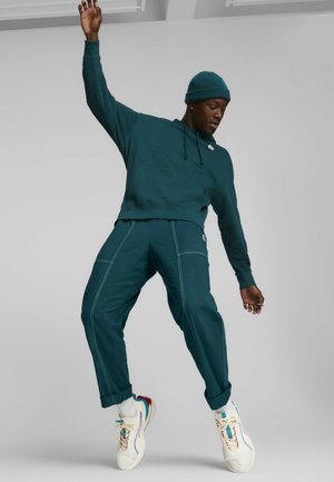 Sudadera azul con bolsillo tipo canguro y puños de canalé, combinada con pantalones azules que tienen costuras blancas. Zapatillas blancas con acentos de color.