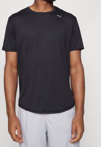 Czarna krótkoszrostowa koszulka sportowa wykonana z gładkiego materiału. Posiada małe logo Pumy na górnej lewej stronie i luźny krój.