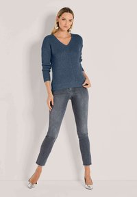 Blauwe gebreide trui met een V-hals en geribbelde textuur. Gepaard met slim-fit, vervaagde grijze jeans en zilveren hoge hakken.