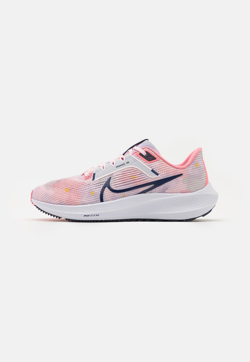 Chaussure de course Nike rose clair avec un swoosh bleu foncé, une semelle intermédiaire blanche et de petits accents jaunes, montrée de profil sur fond blanc.