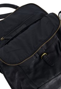 Black leather backpack featuring a gold zipper, exterior zip pocket, and smooth texture with a folded flap design. Interior lined in black fabric.