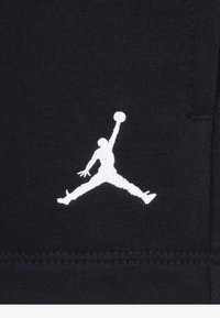 Tela negra con un logo de Jordan bordado en blanco que representa una silueta en una pose de salto, mostrando un diseño atlético y una textura elegante.